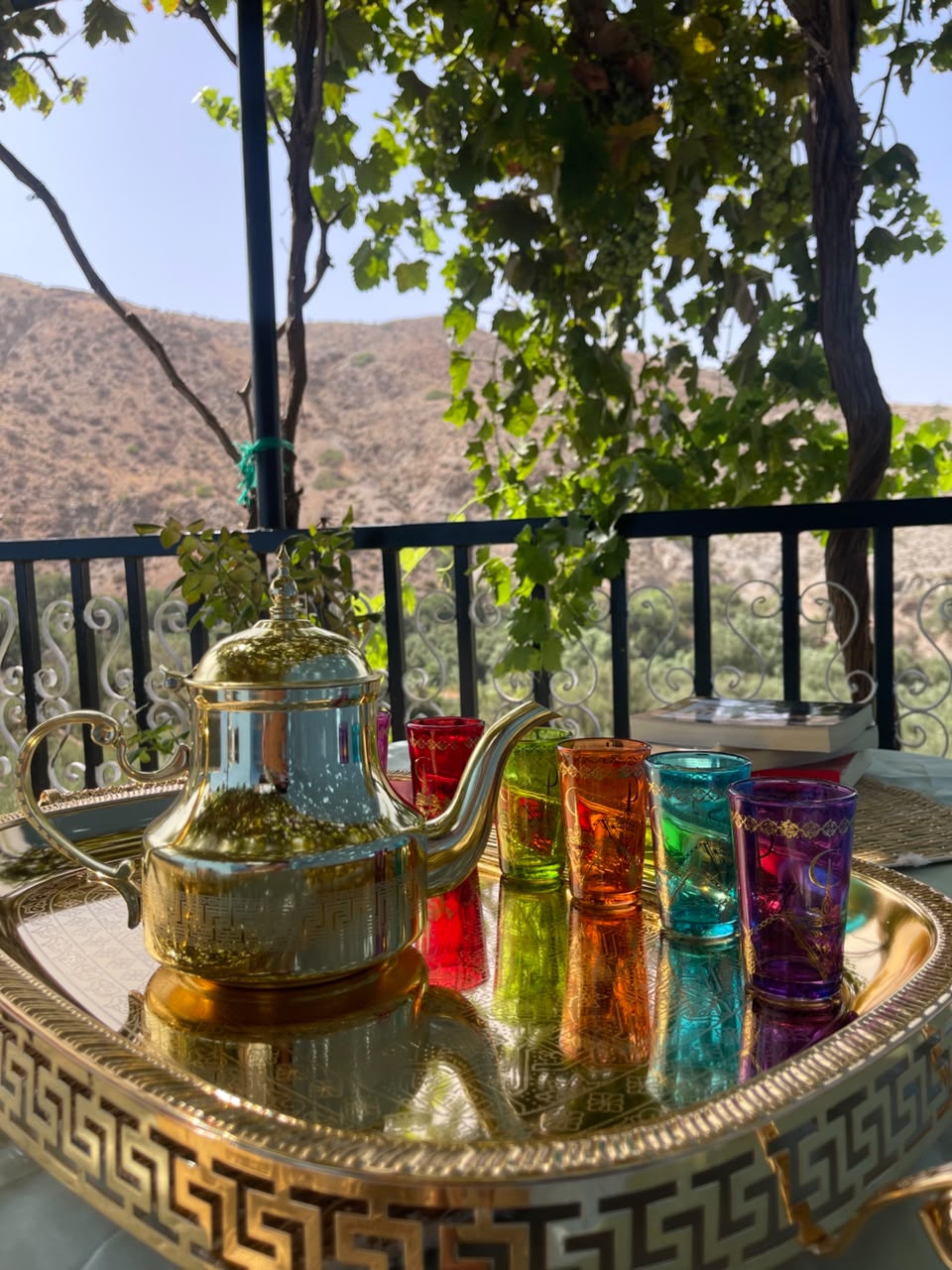 Service à thé marocain doré et verres colorés sur la terrasse, vue sur les montagnes de l'Atlas