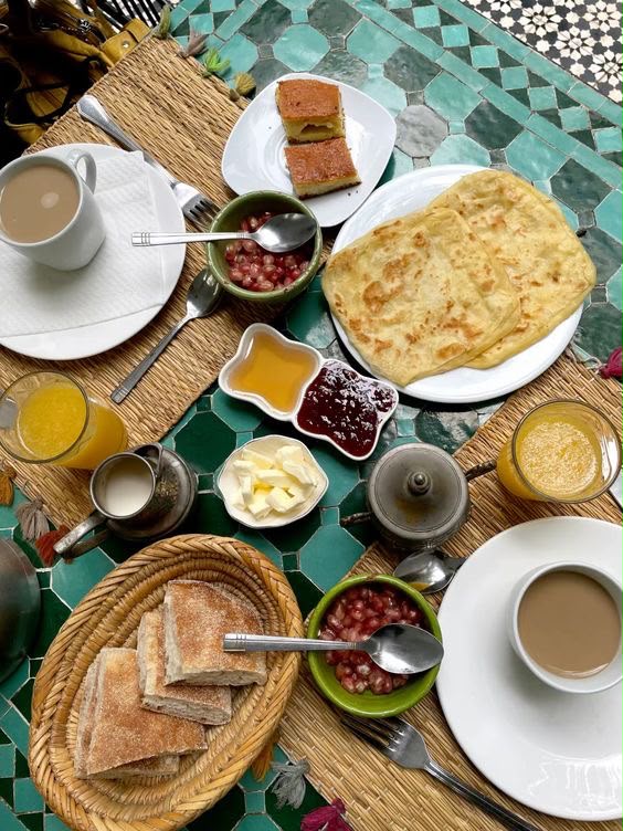 Petit-déjeuner marocain servi sur une table en zellige : msemen, confitures, jus d'orange et café, Tayri Aura