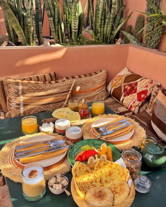 Table de petit-déjeuner dressée dans un patio avec coussins berbères et plantes, Tayri Aura